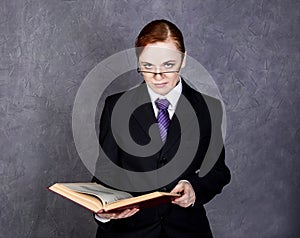 Female lawyer reads a big book with serious expression, woman in a man`s suit, tie and glasses