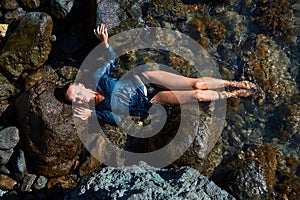 Female laying on sea rock. Lady in wet blue dress. Summer time and relax. Beach vacation. Relaxation and meditation