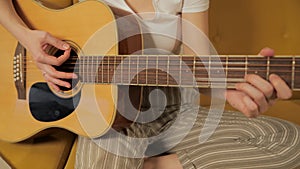 Female learning to play guitar at home. Close up of happy smiling young woman play guitar sitting on coach. Girl bad
