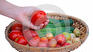 Female left hand Hold the tomato in your hand. Bamboo basket put available fruits and vegetables like cucumber and tomato on white