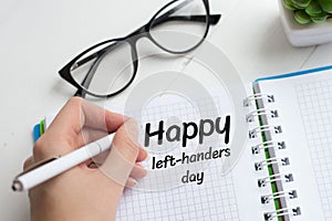 The female left hand writes with a pen in a notebook congratulations on the day of the lefthander