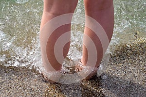 Female legs ashore in sea water and sand