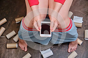 Female legs on the background of the remnants of toilet paper and a phone in her hands. Concept stomach disease, poisoning and