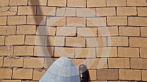 Female legs in blue jeans walk along a street paved with yellow brick, first-person view