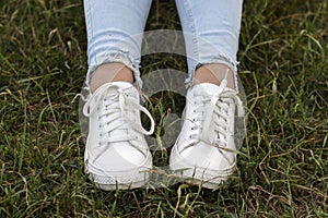 Female legs in blue jeans and white sneakers on green grass.