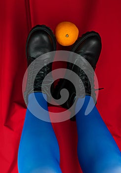 Female legs in blue tights black boots upside down on red background. Fashion modern style. Vivid contrasting colors