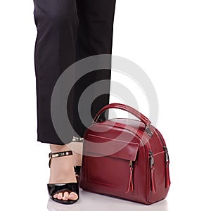 Female legs in classic black pants black lacquer shoes with red leather handbag in hand