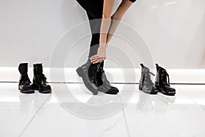 Female legs in fashionable leather black autumn boots in stylish black jeans. Trendy girl stands in a store and measures shoes.