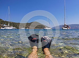 Female legs in flippers in the blue-turquoise crystal clear water on the background of Antisamos beach, Sami Kefalonia island,