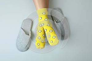 Female legs in funny socks on gray background with slippers