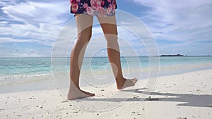 Female legs go on sea beach n Maldivian island. Pure ocean water of Maldives