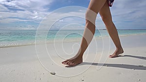 Female legs go on sea beach n Maldivian island. Pure ocean water of Maldives