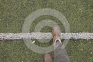 Female legs in gray pants and brown boots stand on a green lawn and lay a dividing strip