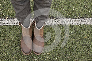 Female legs in gray pants and brown boots stand on a green lawn and lay a dividing strip