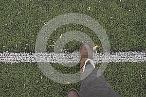 Female legs in gray pants and brown boots stand on a green lawn and lay a dividing strip