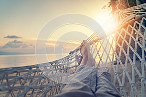 Female legs in a hammock on a background of the sea, palm trees and sunset. Vacation concept, point of view