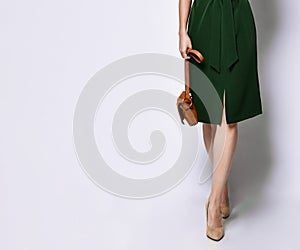 Female legs in high-heeled shoes in a green dress from the designer and brown women`s handbag on a white background