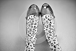 Female legs in leopard print tights and patent leather shoes on a bed. BW photo