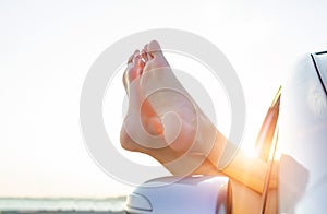 Female legs out of a car window on a background of sky.