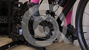 Female legs are pedaling on indoor stationary bicycle trainer. Chain  chainring