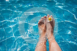 Female legs in the pool water and flower