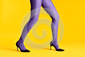 Female legs in purple tights and high heels shoes on yellow background