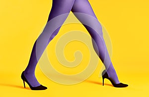 Female legs in purple tights and high heels shoes on yellow background