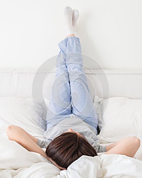 Female legs raised up high and arms under her head lying on bed in bedroom wearing pajamas