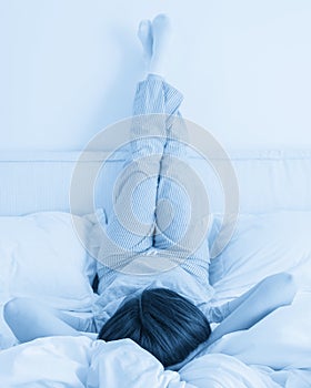 Female legs raised up high and arms under her head lying on bed in bedroom wearing pajamas