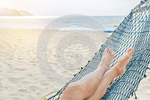 Female legs relaxing on hammock at sandy tropical beach in summer holidays