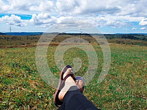 Female legs sitting on the green grass blue cloudy sky green hills