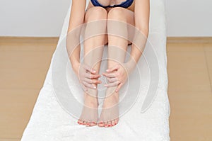 Female legs, sitting on massage couch, hugged her legs with hand