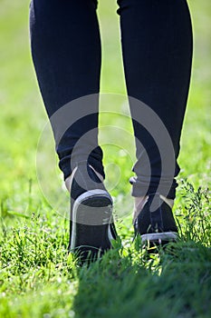 Female legs in sneakers, black sportive tights striding along grass, rear view