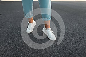 Female legs in stylish blue pants in white leather sneakers on the asphalt in the city. Trendy young woman on a walk. Fashionable