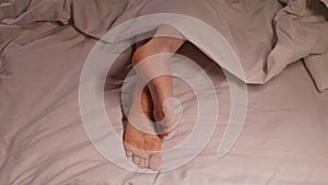 Female legs and toes itch and scabies in the evening in bed on a sheet under a blanket. Woman girl with bare feet foot