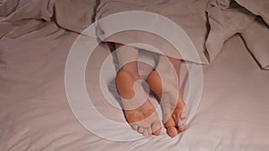 Female legs and toes itch and scabies in night in bed on a sheet under a blanket. Woman girl with bare feet foot with