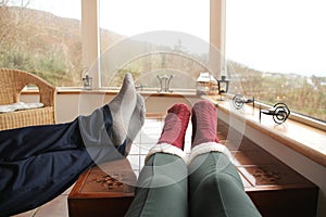 Female legs in warm high socks with fur and male legs on a light closed veranda in the mountains, concept chillin and relaxation