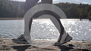 Female legs wear sneakers close up running along coast.