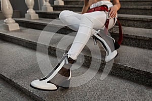 Female legs in white pants with leather fashion shoes and a red bag sits on the street
