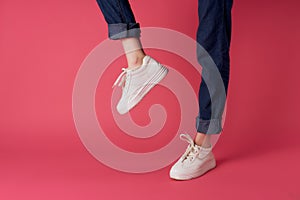 female legs in white sneakers in fashion posing pink background