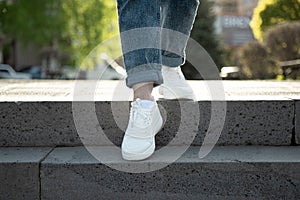 Female legs in white summer sneakers and rolled up jeans descending the stairs in the city . Front view