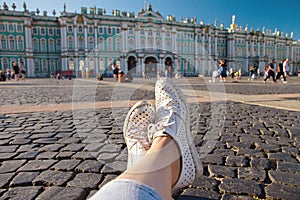 Female legs in worn white macasinas on Palace Square in St. Petersburg, first-person view