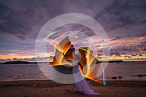 Female light painting model on sandy Tanjung Layar Beach during colorful cloudy sunrise photo