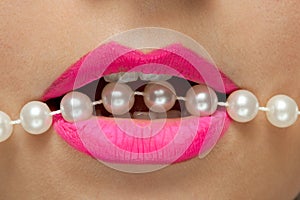 Female lips with pink lipstick and pearls thread.