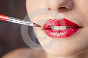 Female lips with red lipstick close-up. Makeup artist applying lipstick with a brush