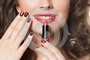 Female lips and red lipstick in hand with dark red manicured nails. Beauty and cosmetic concept, close up beauty portrait