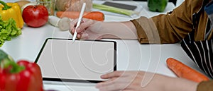 Female looking recipe on mock-up tablet while preparing fresh vegetables ingredients