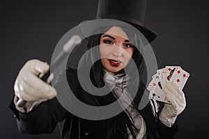 Female magician in performer suit with magic wand and playing ca