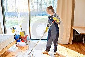 Female maid in blue uniform cleaning floor in bedroom