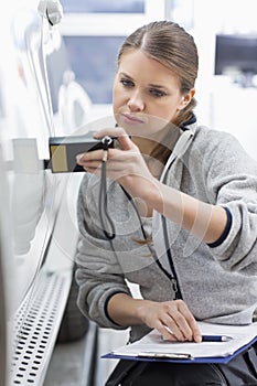 Female maintenance engineer checking car paint with equipment in workshop